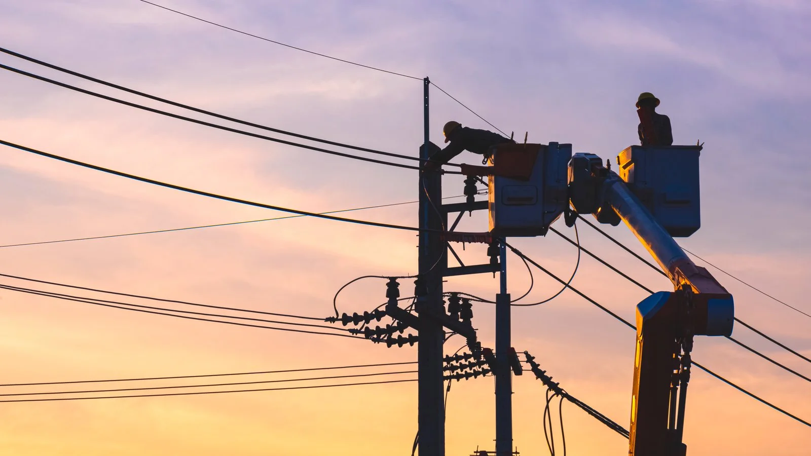 Técnicos en camión canasta trabajando sobre una red eléctrica al atardecer
