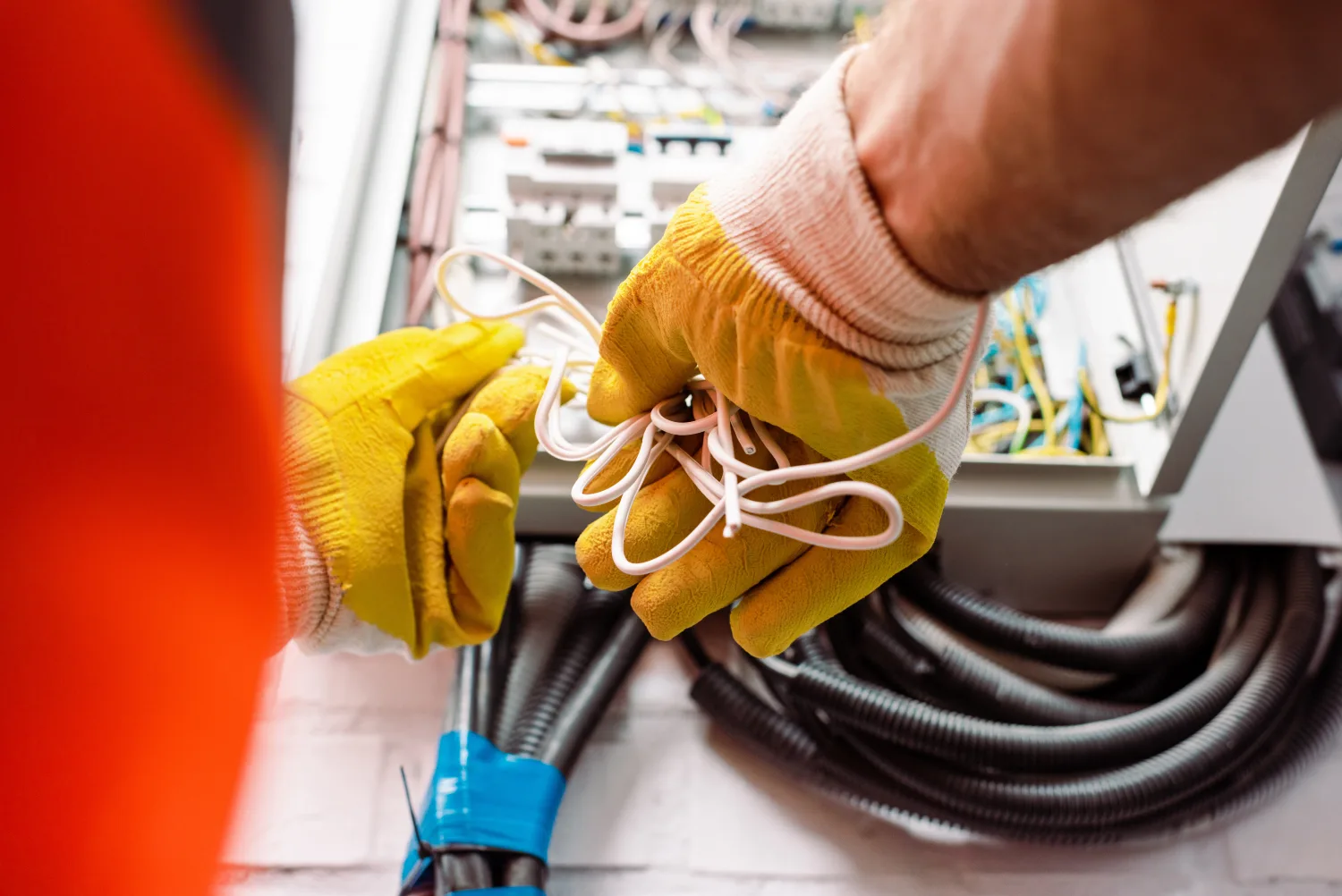Electricista con guantes de trabajo manipulando conductores frente a un tablero